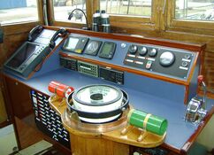 Innenansicht des Steuerhauses auf der Banjaard: Bedienfeld mit Navigationsinstrumenten, Kommunikationsgeräten und Gashebelsteuerung, alles in Holz eingefasst.