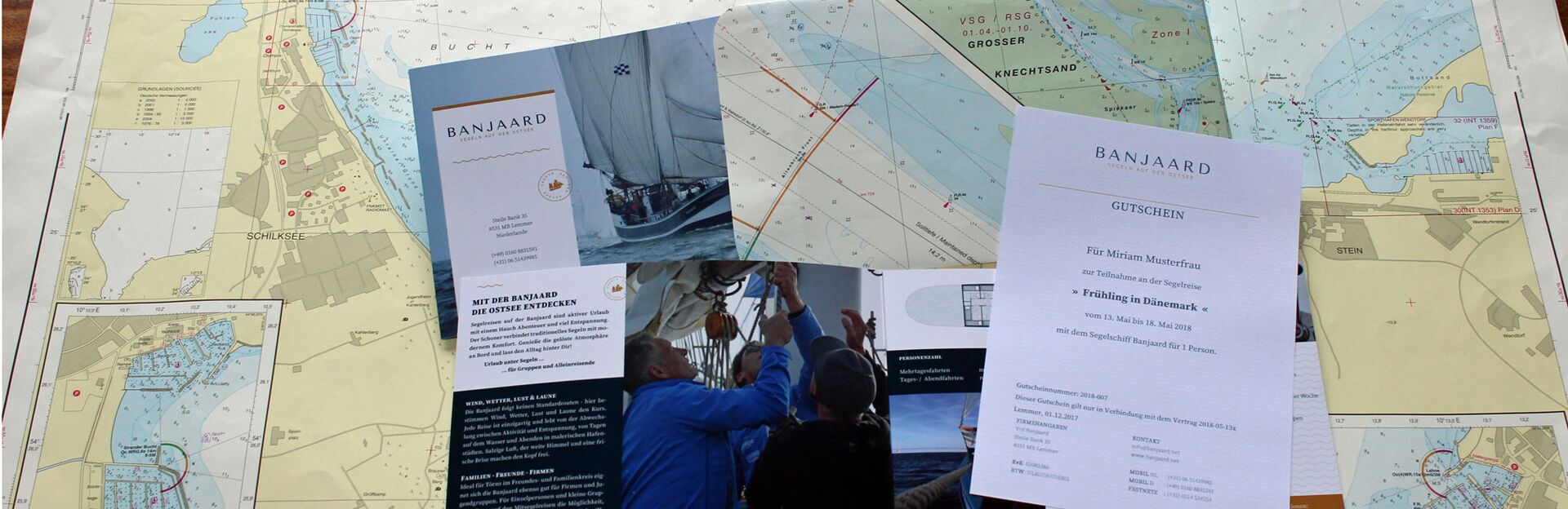 Ein Segelgutschein für eine Reise mit dem Segelschiff Banjaard zusammen mit der Schiffsbroschüre und in einem Umschlag aus einer alten Seekarte.
