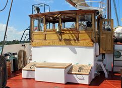 Das Steuerhaus aus Holz auf dem Segelschiff Banjaard mit der Schiffsglocke und einem Holzschild mit der Aufschrift "19 Banjaard 13". Davor stehen zwei Holzluken, einer weißen Kiste mit Holzdeckel und auf beiden Seiten den Treppen zum Achterdeck.