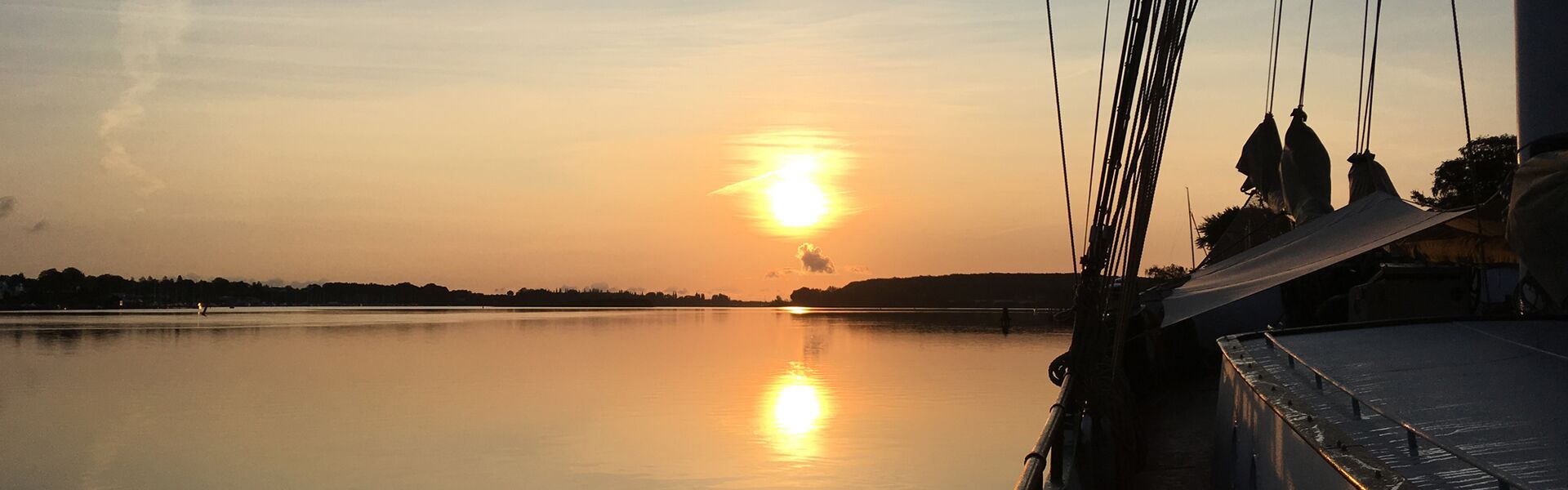 Ein ruhiger Sonnenaufgang im Herbst über dem Svendborg Sund mit der Banjaard am rechten Rand des Bildes. Warm-rötlich scheint das Licht, im leichten Frühnebel ist das Bild der Sonne und ihrer Spiegelung im Wasser verzerrt.