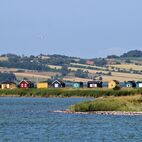 Bunte kleine Strandhäuser auf einer Halbinsel vor dem Hintergrund einer ansteigenden Küste mit Bäumen, Sträuchern und hellen Feldern in der Nähe von Ærøskøbing,