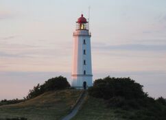 Der weiße Leuchtturm Dornbusch auf Hiddensee bei einsetzender Dämmerung vor einem sich rosa färbenden Himmel
