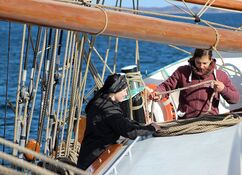 Ordnung auf einem Segelschiff: zwei junge Frauen räumen an Deck ein Tau auf, indem sie es in großen Schlaufen ordentlich aufeinander legen.