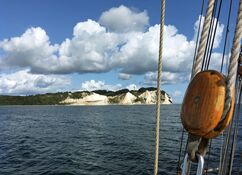 Ein Blick von einem Schiff auf eine Insel mit dramatischen weißen Klippen und üppigem Grün unter einem blauen Himmel mit flauschigen Wolken.