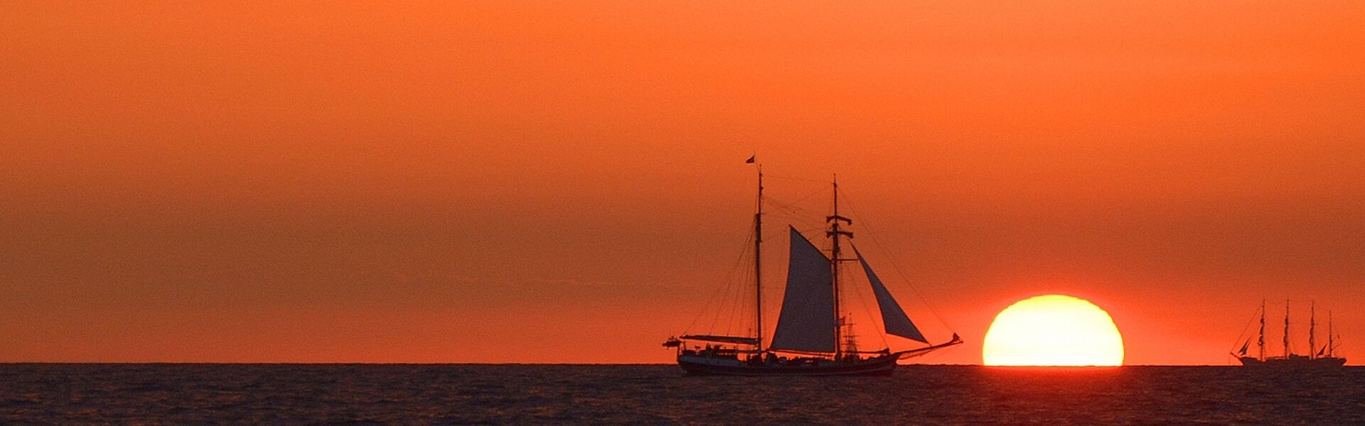 Silhouette des Segelschiffes Banjaard vor einem leuchtend roten Himmel bei Sonnenuntergang vor Warnemünde während der Hanse Sail.