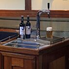 Kleine Bar im Salon der Banjaard an der neben zwei Weinflaschen ein frischgezapftes Bier unter dem Zapfhahn steht.