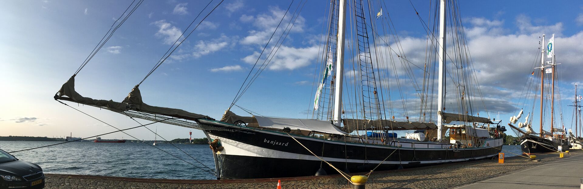 Eine ruhige maritime Szene am Tiessenkai in Kiel-Holtenau mit dem Segelschiff Banjaard. Alle Segel sind eingepackt, das Deck aufgeräumt, das Schiff wartet auf die nächsten Gäste. Rechts sind zwei weiter Schiffe zu sehen.