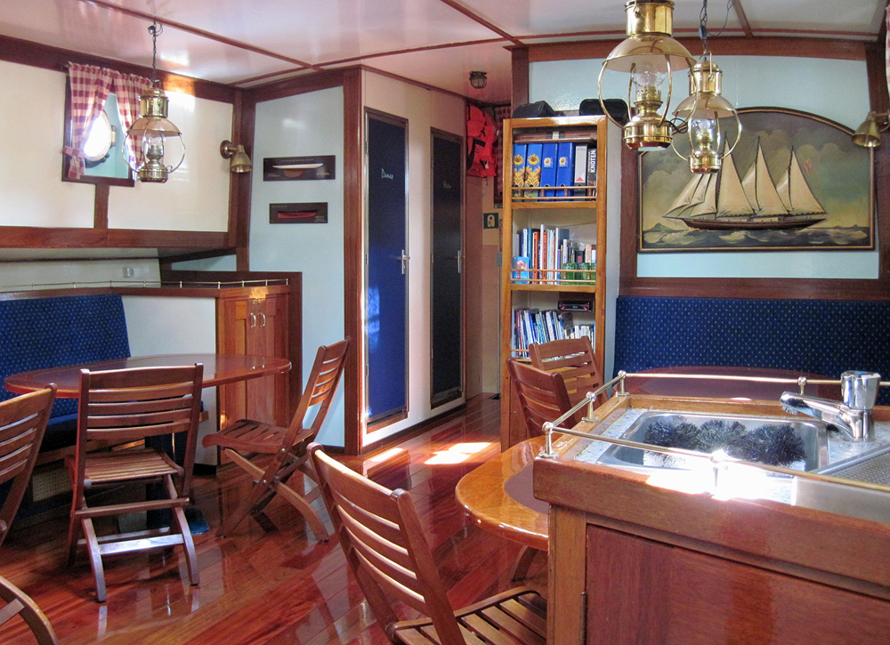 Salon Banjaard mit Tischen, Stuehlen, Sitzbaenken, Bordbibliothek und kleiner Bar